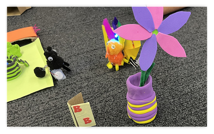 Student maker projects including a foam flower in a clay vase.