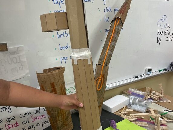 A cardboard skyscraper in the shape of a cylinder. Circular cardboard figures are attached to the sides. Masking tape holds the cylinders together.
