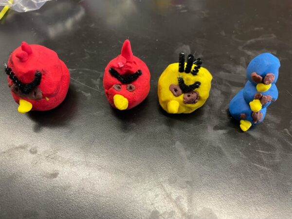 Four small clay Angry Bird figurines. Two are red, one is yellow, and three smaller blue ones are stacked on top of each other.