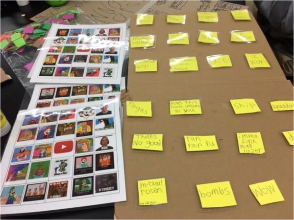 Three laminated pages of thumbnails of memes sits beside a long piece of cardboard with yellow stickies arranged in an array. A word or phrase is written on each sticky.